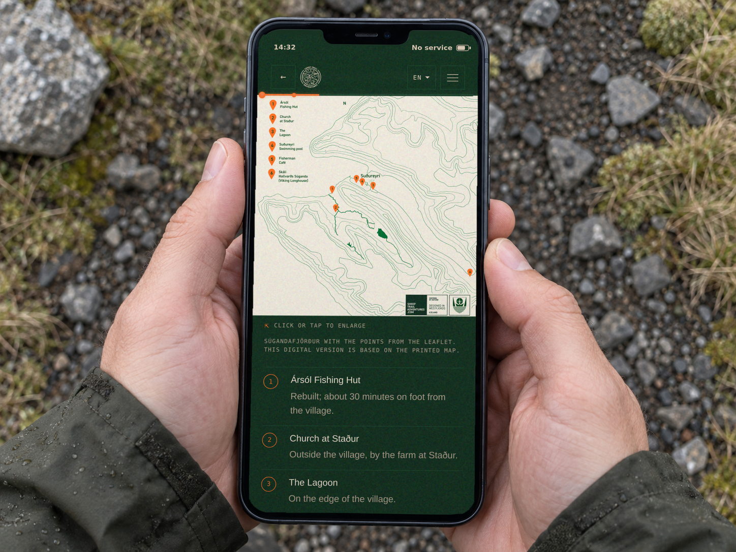 Hands holding a phone with the Suðureyri guide open; the screen shows a map of Súgandafjörður and a status bar with no service.