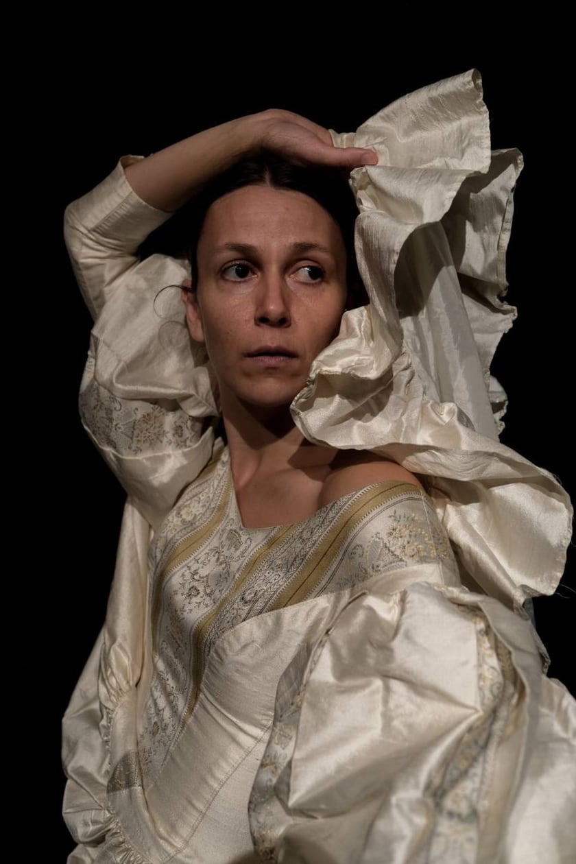 An actress in a light, flowing costume poses against a black background.