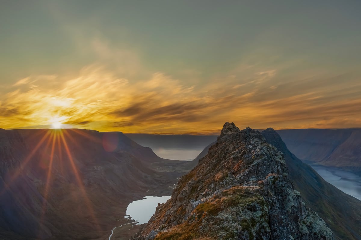 The Sun low over the Westfjords ridges, with a lake and a valley running down to the fjord below.