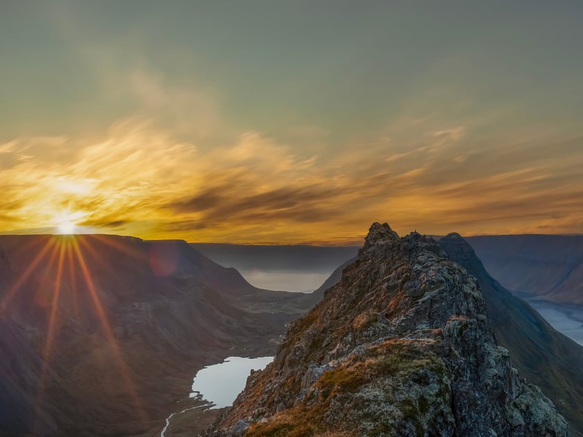 The Sun low over the Westfjords ridges, with a lake and a valley running down to the fjord below.