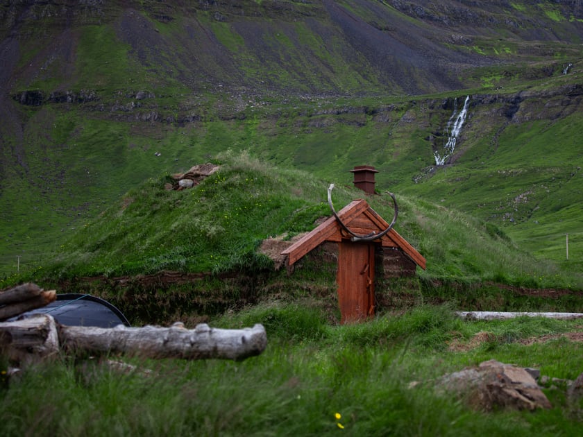 A turf-roofed hut with a wooden door and whale jawbones above the entrance, a green slope with a waterfall behind.