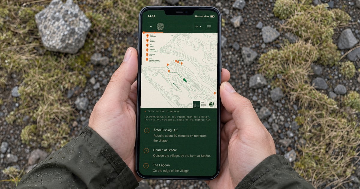 A phone held in two hands with the Suðureyri guide open; the screen shows a map of the fjord with marked places and a no-service indicator.